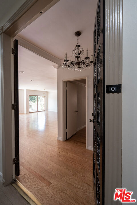 corridor featuring wood-type flooring and an inviting chandelier