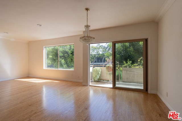 empty room with a chandelier, ornamental molding, and light wood-type flooring