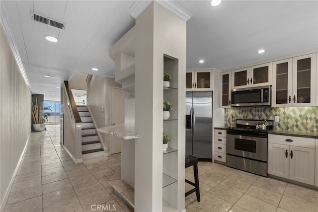 kitchen featuring decorative backsplash, ornamental molding, appliances with stainless steel finishes, and dark stone counters