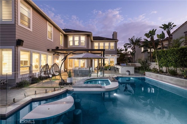 pool at dusk with a patio area and an in ground hot tub