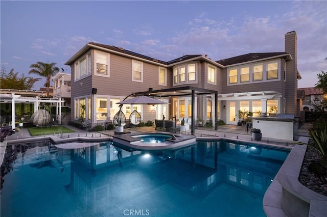 back house at dusk with a swimming pool with hot tub, a patio area, and exterior kitchen