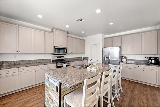 kitchen featuring light stone counters, stainless steel appliances, a breakfast bar, a sink, and an island with sink