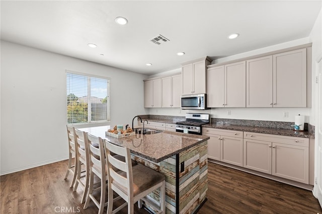 kitchen featuring visible vents, appliances with stainless steel finishes, dark stone countertops, dark wood-style flooring, and a sink