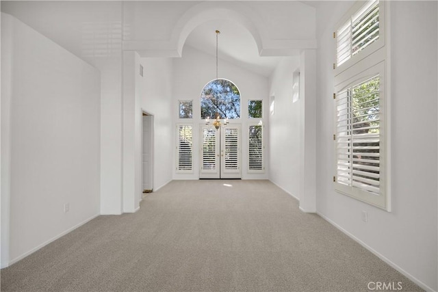 empty room with high vaulted ceiling, light carpet, and a notable chandelier