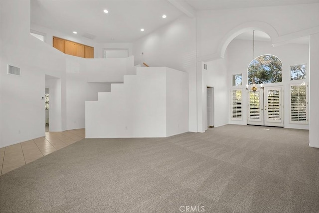 unfurnished living room with light colored carpet, beamed ceiling, and a towering ceiling