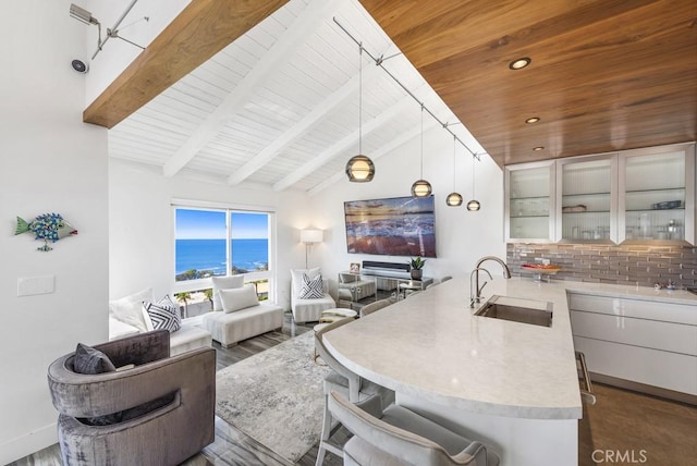 kitchen with white cabinets, vaulted ceiling with beams, tasteful backsplash, sink, and hanging light fixtures