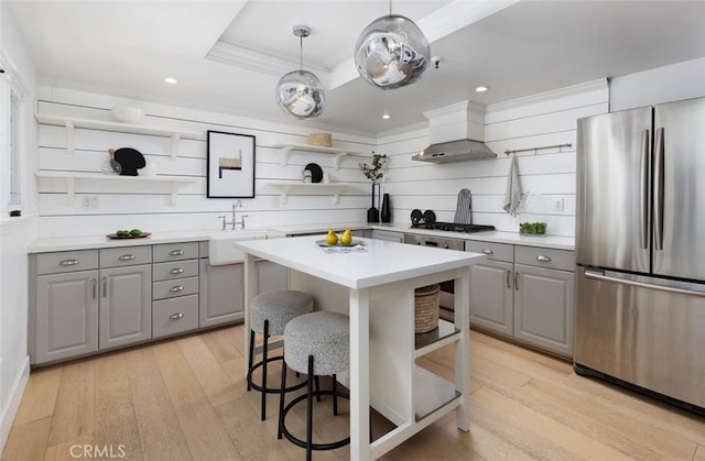 kitchen featuring decorative light fixtures, wall chimney range hood, a kitchen island, sink, and appliances with stainless steel finishes