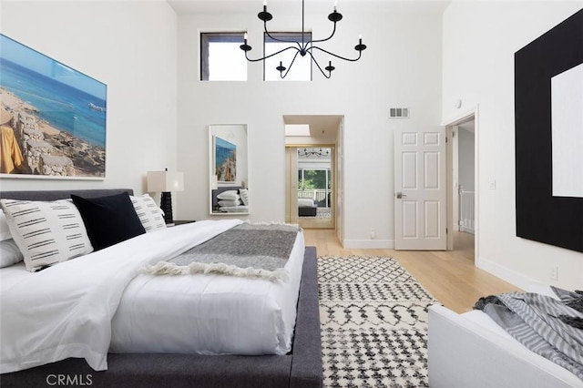 bedroom with light wood-type flooring, a towering ceiling, and a notable chandelier