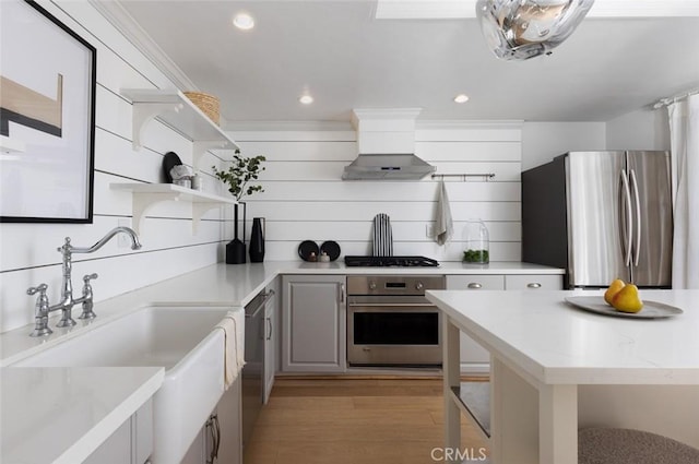 kitchen featuring appliances with stainless steel finishes, wall chimney exhaust hood, sink, gray cabinets, and light wood-type flooring