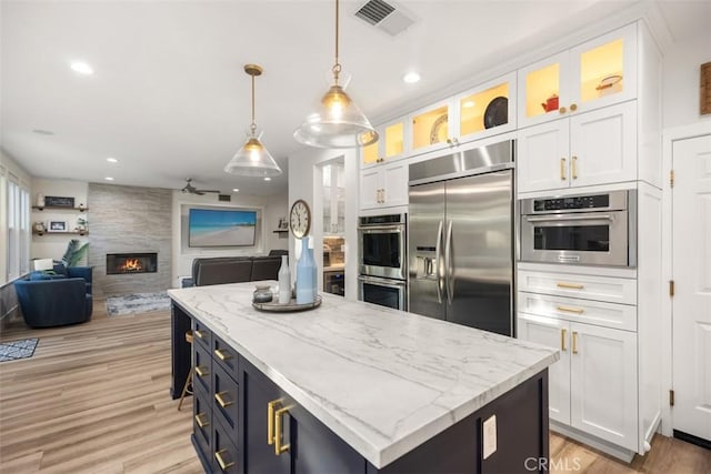 kitchen with white cabinetry, a center island, a large fireplace, pendant lighting, and stainless steel appliances