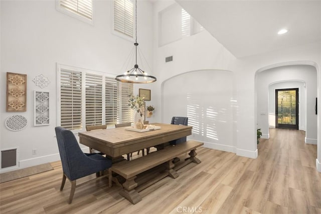 dining room with a notable chandelier, a towering ceiling, and light hardwood / wood-style floors