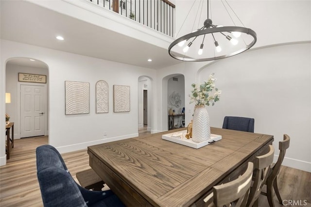 dining room featuring a towering ceiling, a notable chandelier, and light wood-type flooring