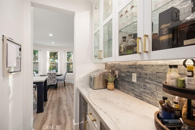 bar with white cabinetry, light stone countertops, decorative backsplash, and light hardwood / wood-style flooring