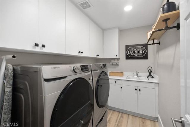 clothes washing area with cabinets, washing machine and dryer, sink, and light hardwood / wood-style floors