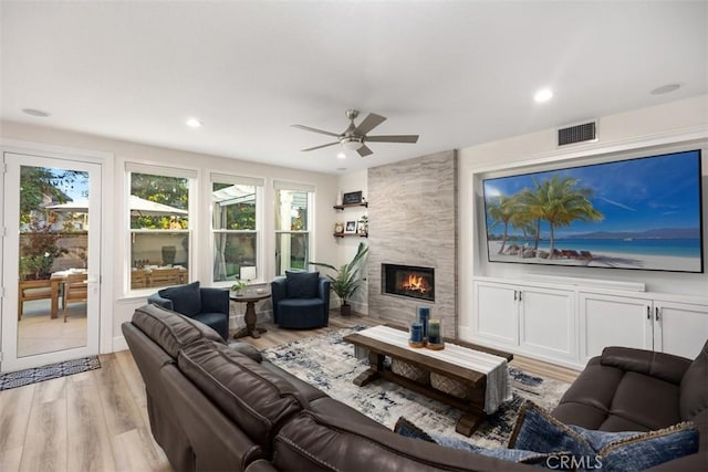 living room with ceiling fan, a tile fireplace, and light hardwood / wood-style flooring