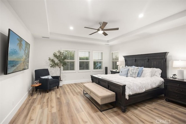 bedroom with ceiling fan, a tray ceiling, and light wood-type flooring