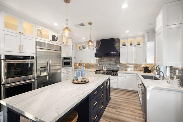 kitchen with appliances with stainless steel finishes, pendant lighting, sink, white cabinets, and custom exhaust hood