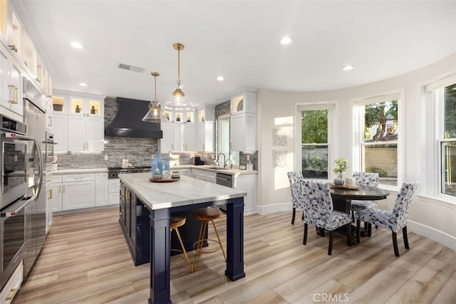 kitchen with white cabinetry, hanging light fixtures, custom exhaust hood, and a kitchen island