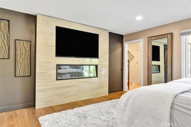 bedroom with ensuite bath, light wood-type flooring, and a tile fireplace