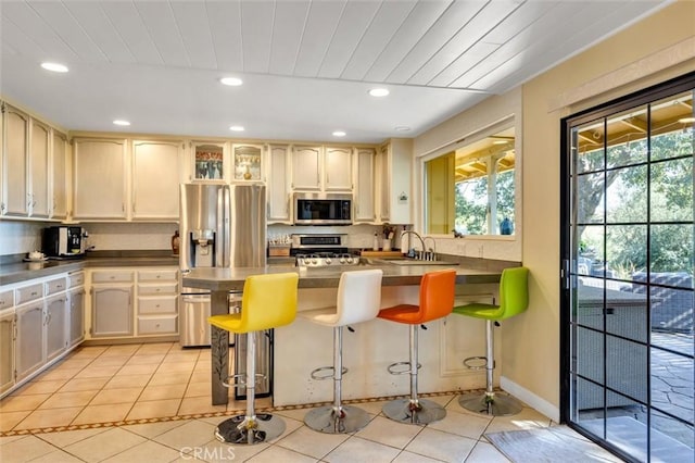 kitchen with light tile patterned floors, a kitchen bar, stainless steel appliances, cream cabinets, and sink