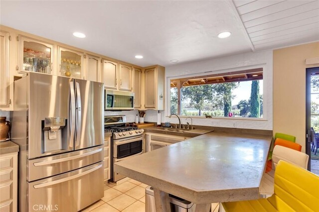 kitchen with stainless steel appliances, light brown cabinetry, sink, kitchen peninsula, and light tile patterned floors