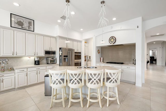 kitchen with a kitchen bar, hanging light fixtures, appliances with stainless steel finishes, and a center island with sink