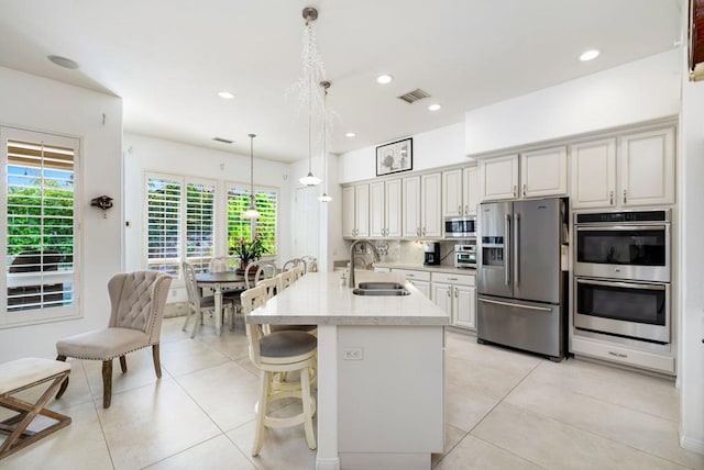 kitchen with appliances with stainless steel finishes, decorative light fixtures, a kitchen bar, sink, and a kitchen island with sink