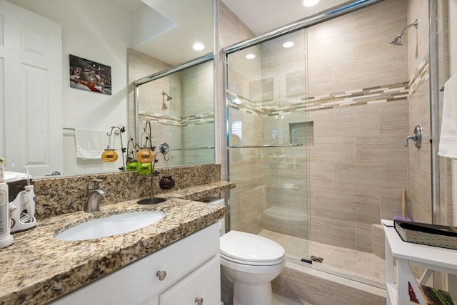 bathroom featuring a shower with door, toilet, and vanity