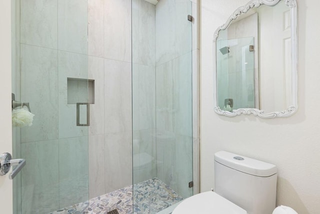 bathroom featuring a shower with door and toilet