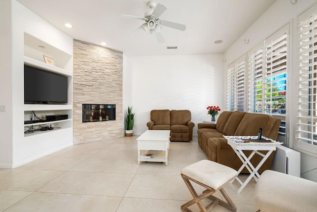 living room with built in features, ceiling fan, light tile patterned floors, and a tiled fireplace