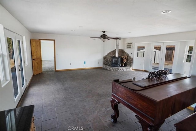 unfurnished living room with ceiling fan, a wood stove, and french doors