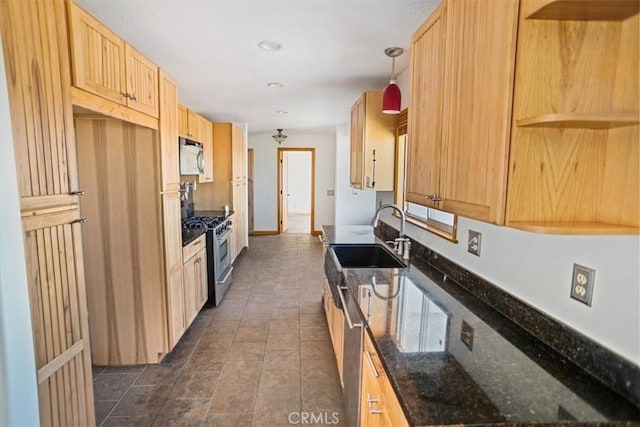 kitchen with light brown cabinets, dark stone counters, sink, hanging light fixtures, and gas range