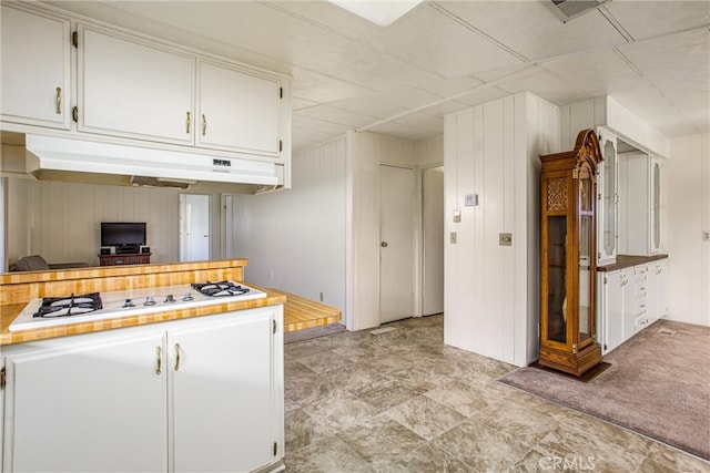 kitchen featuring white gas stovetop, white cabinetry, wooden walls, and light carpet