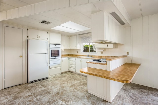 kitchen featuring wood walls, white appliances, sink, kitchen peninsula, and white cabinets