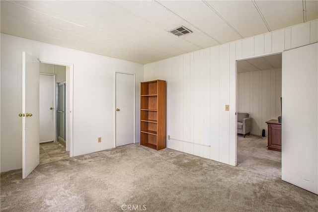 unfurnished bedroom with wooden walls and light colored carpet