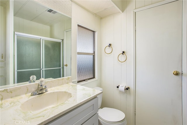 bathroom featuring vanity, wooden walls, toilet, and an enclosed shower