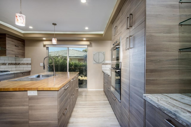 kitchen featuring oven, a kitchen island with sink, wooden counters, and decorative light fixtures