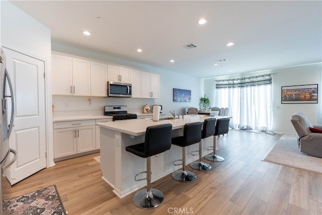 kitchen featuring light hardwood / wood-style floors, a center island with sink, white cabinetry, appliances with stainless steel finishes, and a kitchen bar