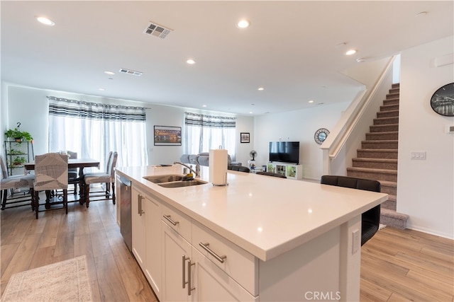 kitchen featuring an island with sink, light wood-type flooring, a healthy amount of sunlight, and white cabinetry