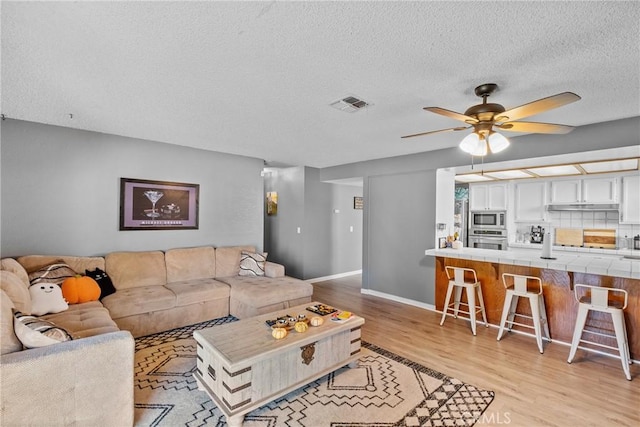 living room featuring a textured ceiling, light wood-type flooring, and ceiling fan