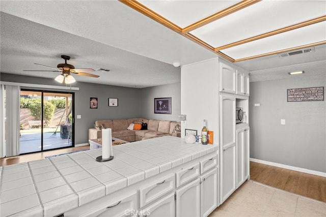 kitchen featuring ceiling fan, tile counters, light hardwood / wood-style flooring, a textured ceiling, and white cabinets