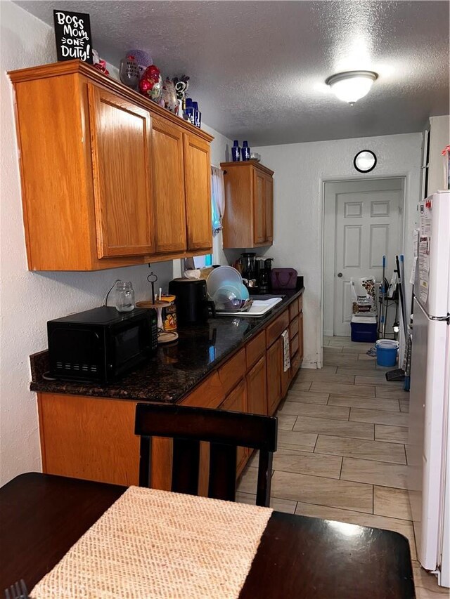 kitchen featuring dark stone countertops, sink, a textured ceiling, and white refrigerator