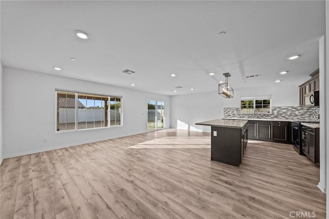 kitchen with light wood-type flooring, backsplash, dark brown cabinetry, a center island, and hanging light fixtures