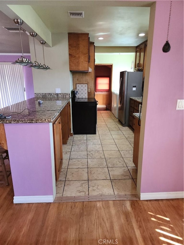 kitchen featuring dark stone countertops, light hardwood / wood-style floors, a kitchen bar, kitchen peninsula, and stainless steel refrigerator