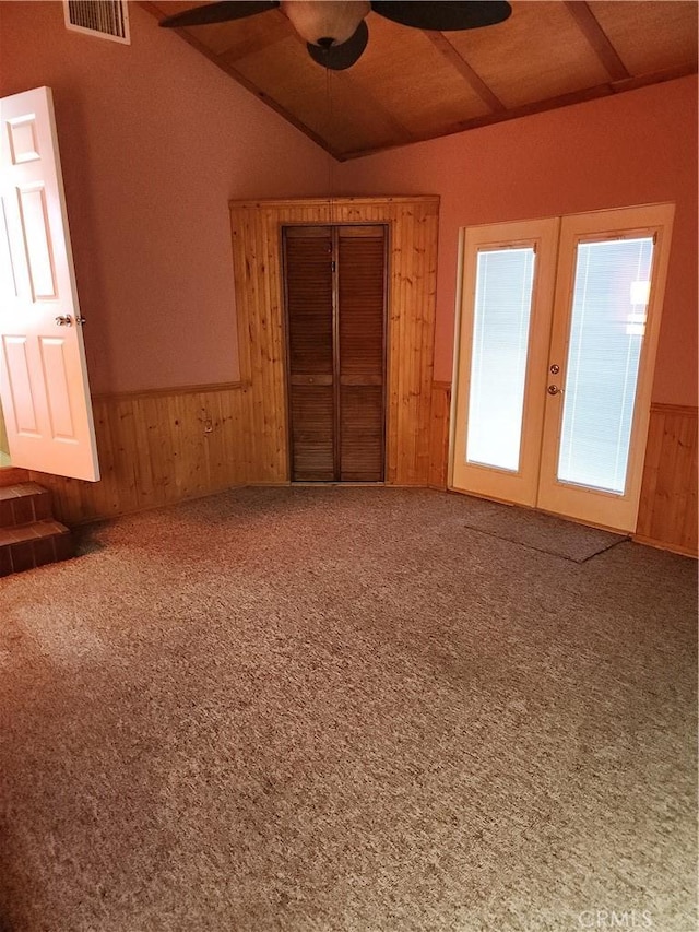 empty room featuring carpet, wood walls, lofted ceiling, french doors, and ceiling fan