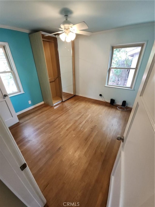 unfurnished bedroom featuring ceiling fan, crown molding, baseboards, and wood finished floors