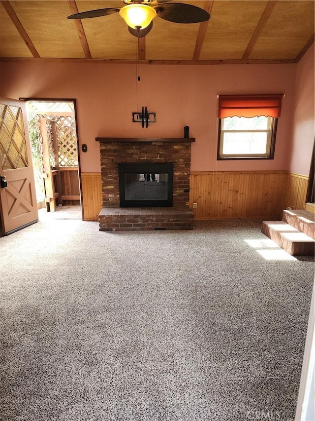 unfurnished living room featuring wooden ceiling, wainscoting, a fireplace, and carpet flooring