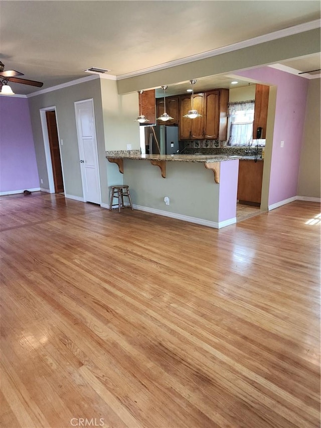 kitchen with brown cabinets, stainless steel refrigerator with ice dispenser, open floor plan, a peninsula, and a kitchen bar