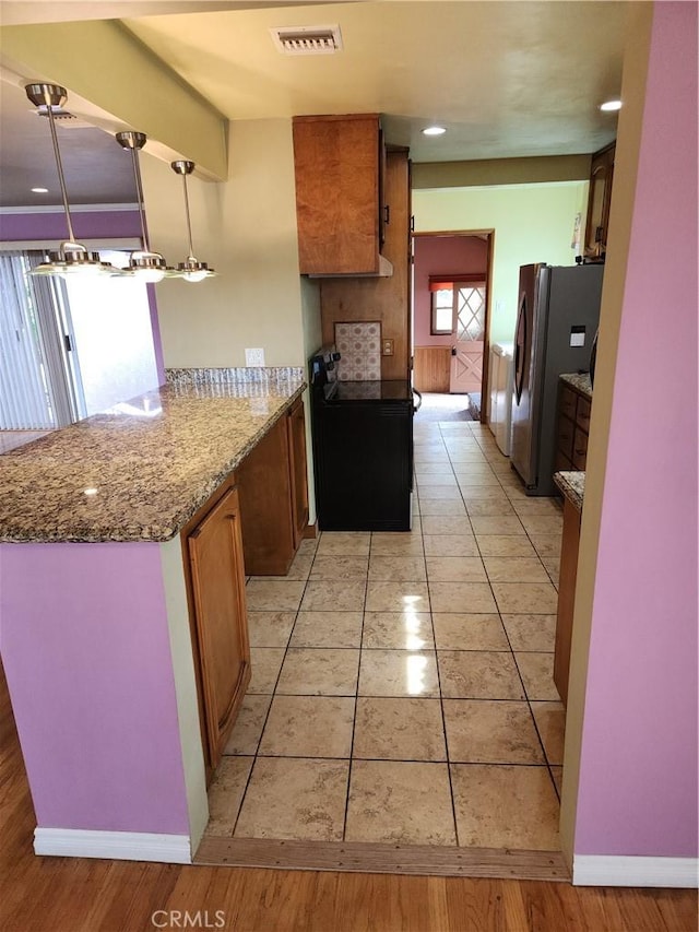 kitchen with black range with electric cooktop, visible vents, freestanding refrigerator, brown cabinets, and pendant lighting