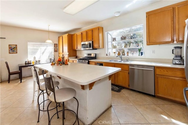 kitchen with appliances with stainless steel finishes, sink, light tile patterned floors, pendant lighting, and a center island